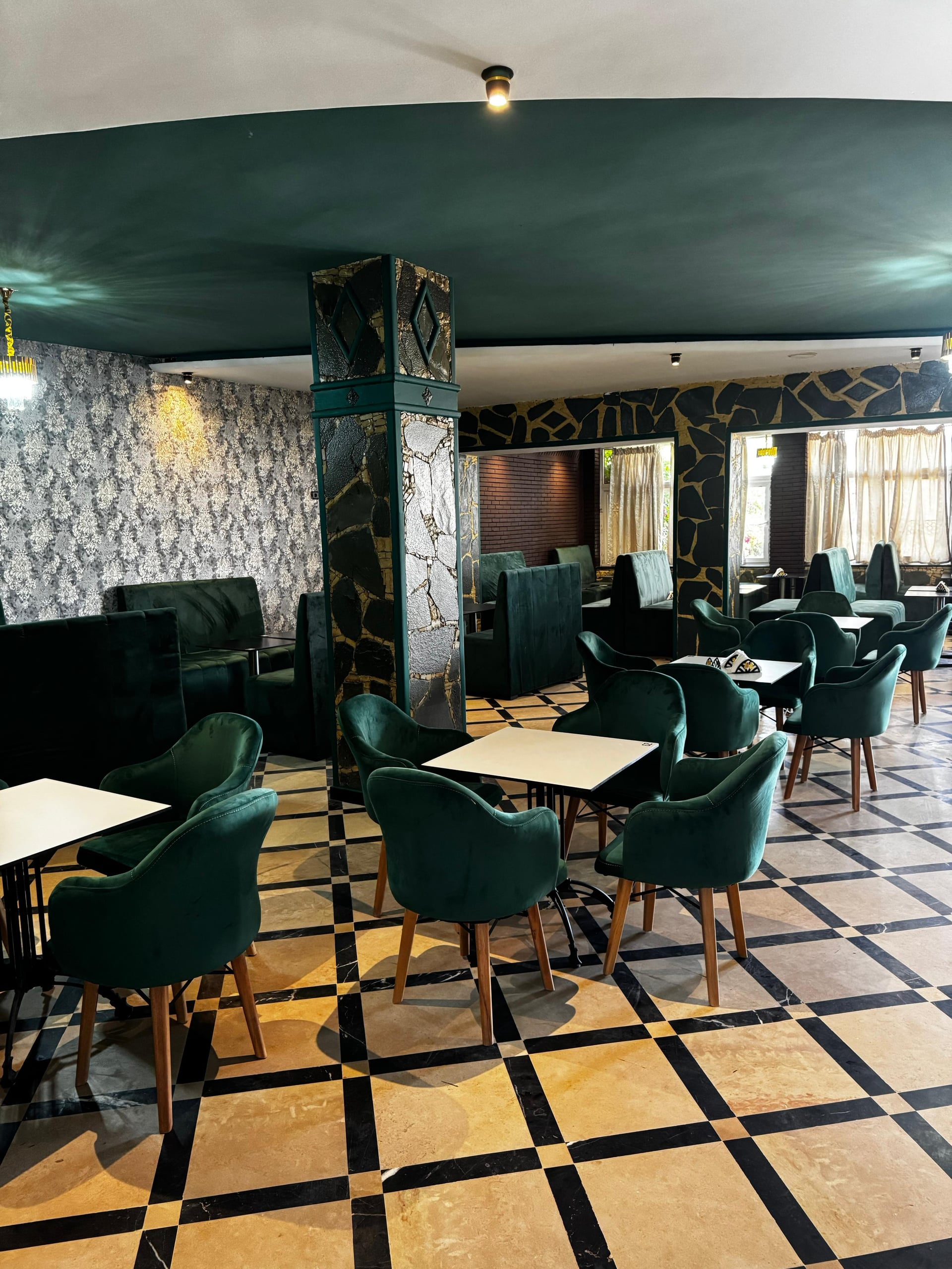 Elegant interior dining room with green velvet armchairs, checkerboard tiled floor, and custom stone columns at Restaurant Bab Aourir